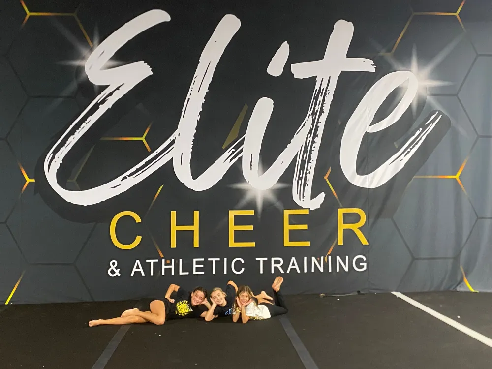 Elite Cheer athletes in front of the Elite Cheer & Athletic Training gym wall